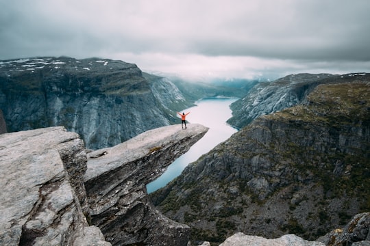 person standing on gray high-rise rock formation at daytime in Trolltunga Norway