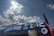 A vintage aircraft with a dark blue fuselage is parked under a bright sky with scattered clouds. The side of the plane features painted artwork and bold white numbers and letters, '212' and 'CHEM-TOOLS'. The artwork depicts a cartoon figure in blue overalls holding a tool. The aircraft canopy is partially visible, and the sunlight creates a dramatic contrast with the clouds.