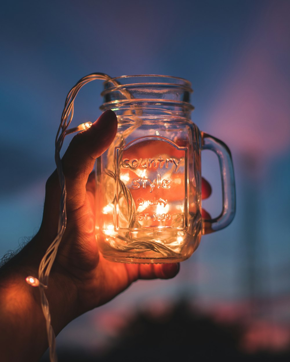 person holding jar with lighted string lights
