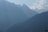 Two paragliders soar through a misty mountain landscape with rugged peaks and scattered clouds. The scene portrays a sense of adventure and tranquility against a backdrop of towering mountains.