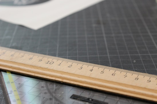 Close-up of a stainless steel cork back ruler resting on a wooden workbench with soft natural light.