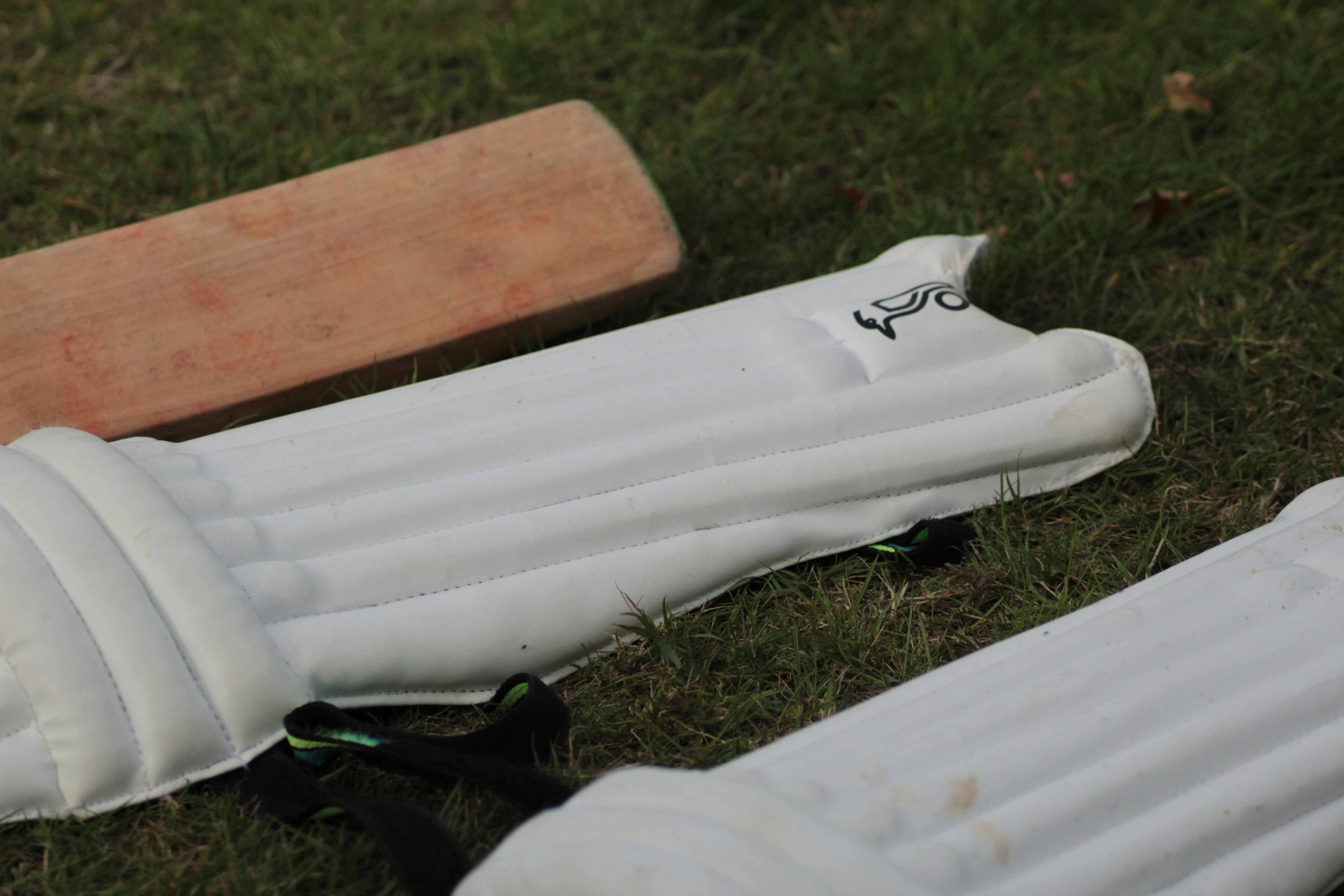 Sports equipment including cricket bat and football on green field