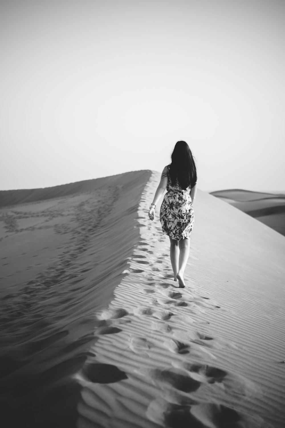 昼間の砂漠を歩く女性のグレースケール写真