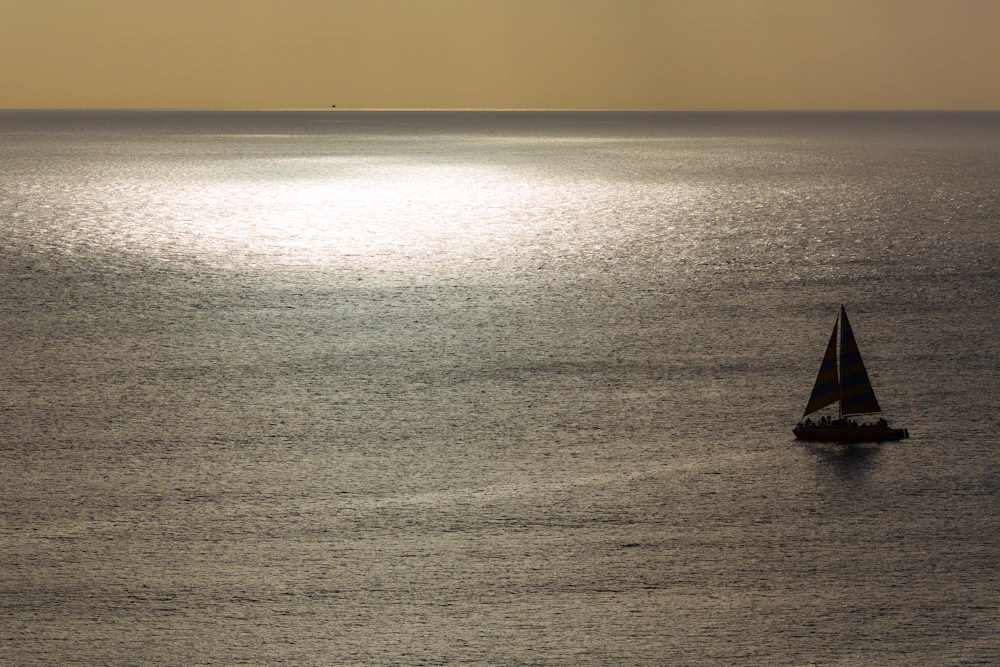 Sailboat silhouetted against the sunset over calm water, similar to Búzios sunset sails