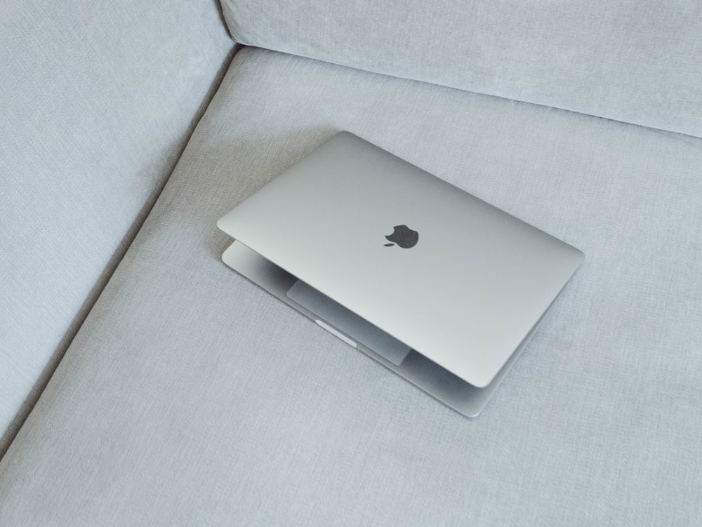silver MacBook on white fabric sofa