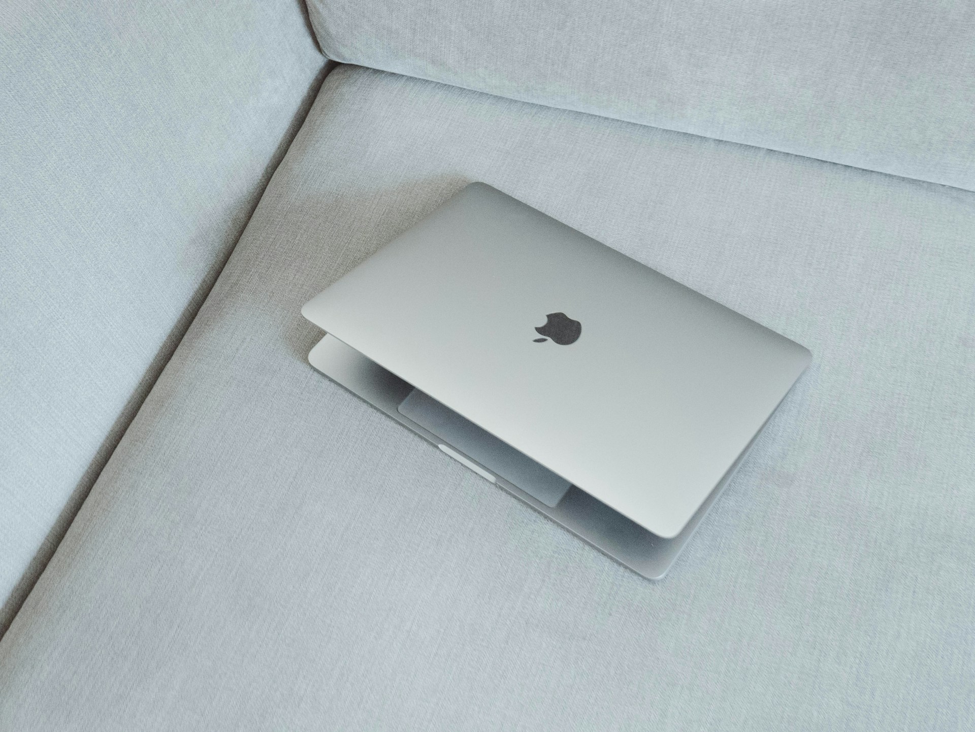 silver MacBook on white fabric sofa