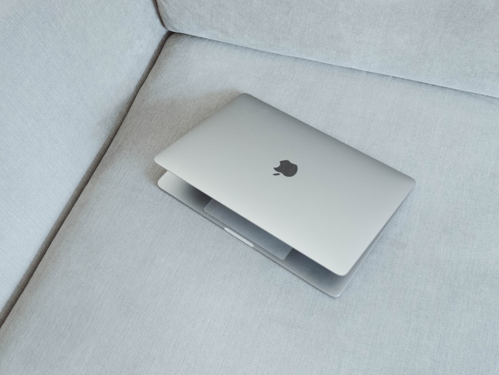 MacBook prateado no sofá de tecido branco