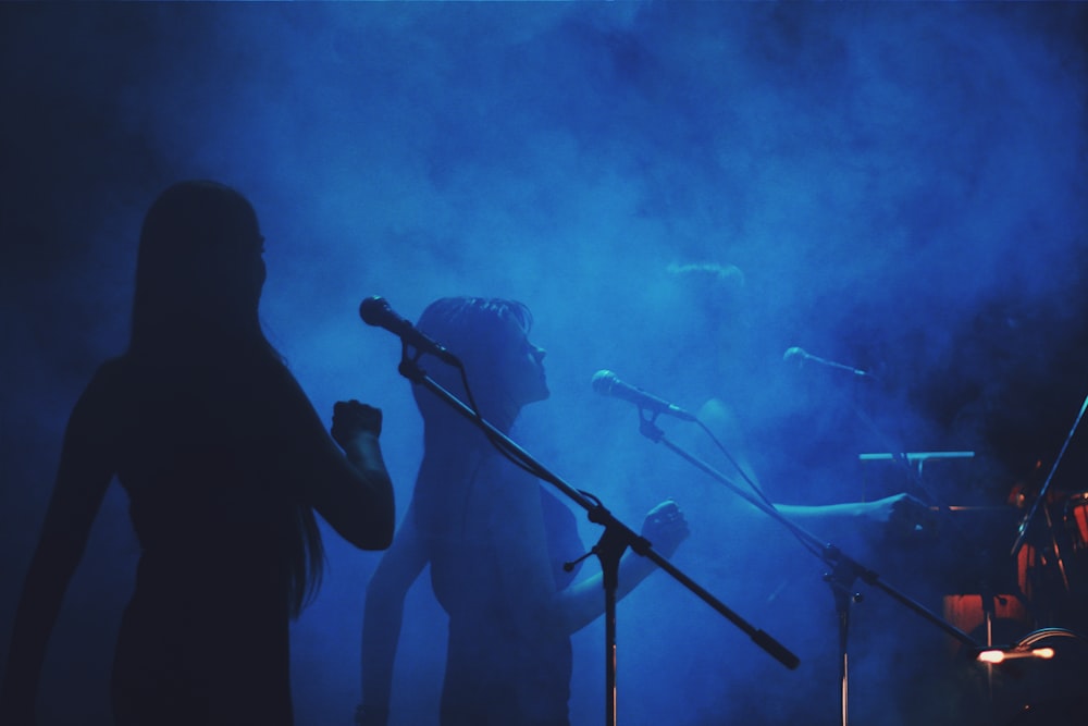 Photographie de silhouette de trois femmes debout devant des pieds de micro