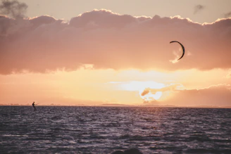 A friendly kite surfer smiling with a kite and ocean backdrop at sunset.
