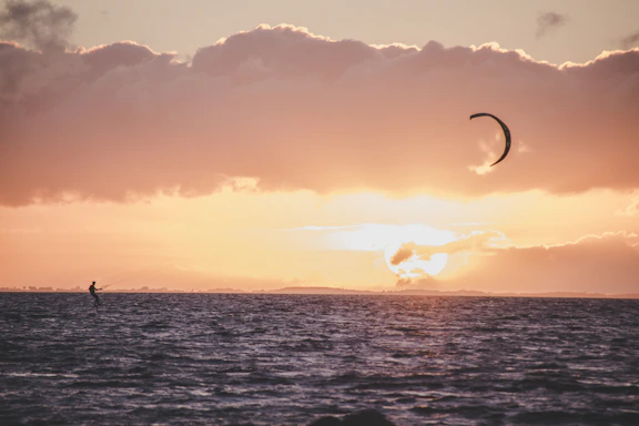 A friendly kite surfer smiling with a kite and ocean backdrop at sunset.