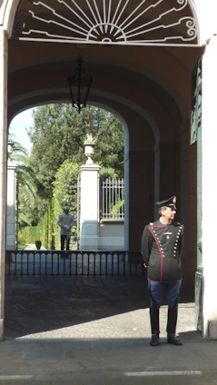 A professional security guard standing alert at the entrance of a modern office building during daytime.