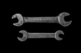 Two metallic open-end wrenches are placed parallel to each other against a black background. The top wrench is slightly larger and has 'MADE IN U.S.A.' engraved on it, while the bottom wrench shows the inscription 'FAIRMOUNT CLEVE'. Both wrenches are weathered, adding a rustic and industrial feel.