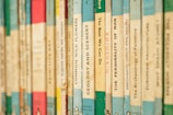 A close-up of a row of vintage paperback books with various titles on their spines. The books are arranged vertically, showing a variety of colors and fonts, giving a nostalgic and scholarly atmosphere.