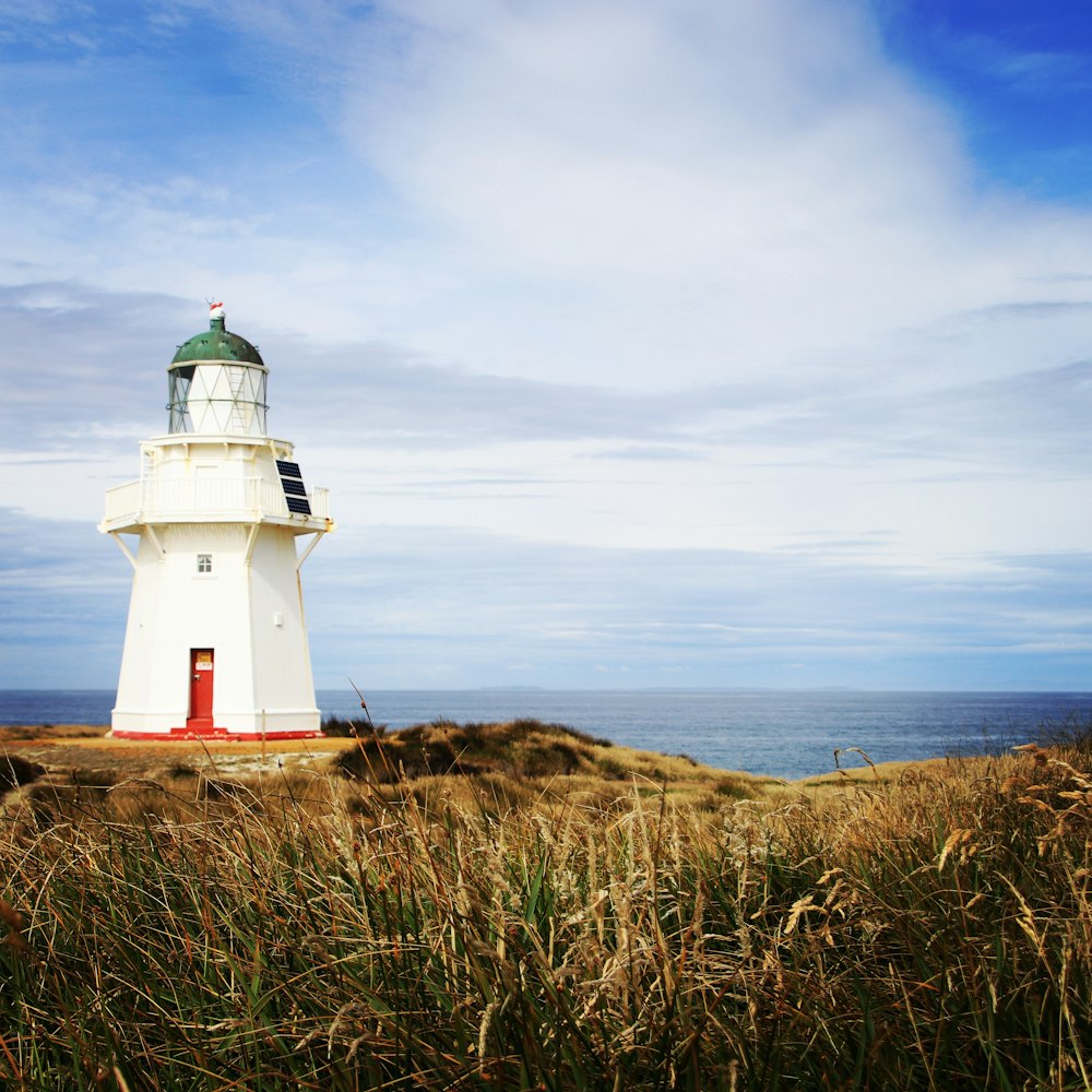 Photo de phare en béton blanc près de l’océan sous un ciel nuageux bleu