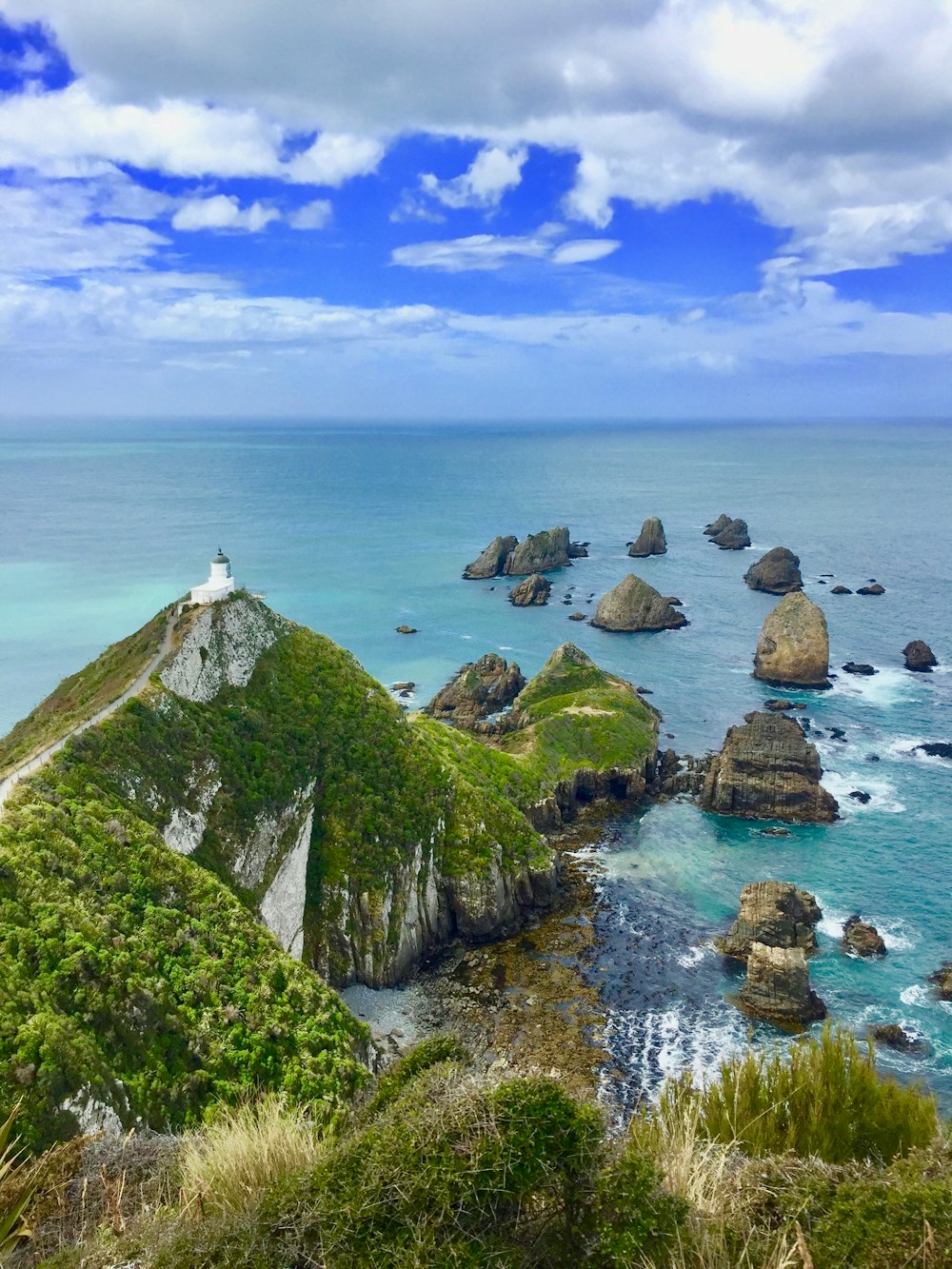 white and green lighthouse on cliff mountain facing body of water