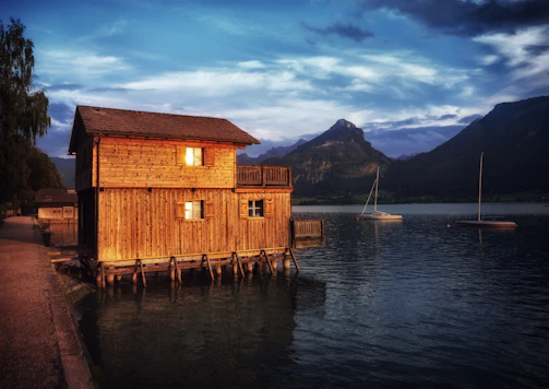 A twilight view of a luxury lakefront timber home with warm interior lights glowing through large windows.