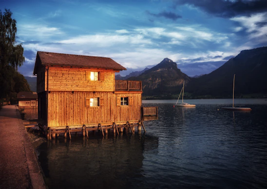 warmly lit handcrafted timber home nestled among pine trees with a reflective lake in the background at golden hour
