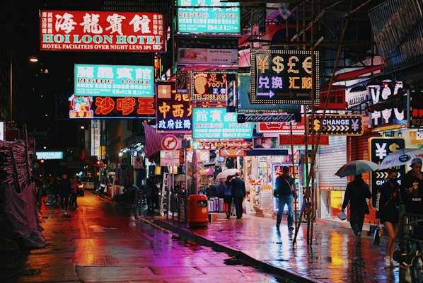 People walking on a wet city street under glowing neon signs in Hong Kong