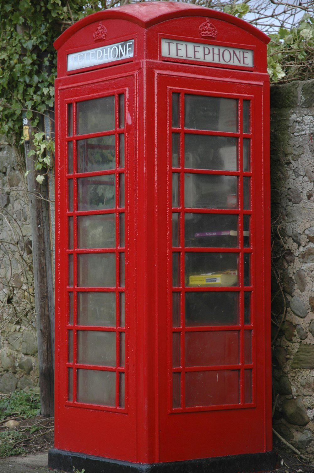 red wooden telephone booth beside gray concrete stonewall at daytime