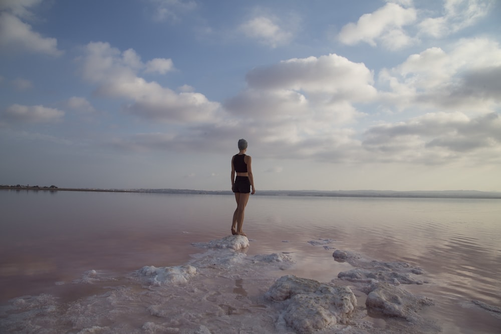 woman standing on top of rock near body of water