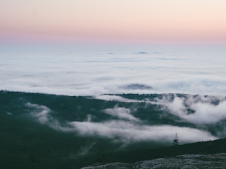 A serene landscape of soft clouds gently drifting over a lush, green valley at sunrise.