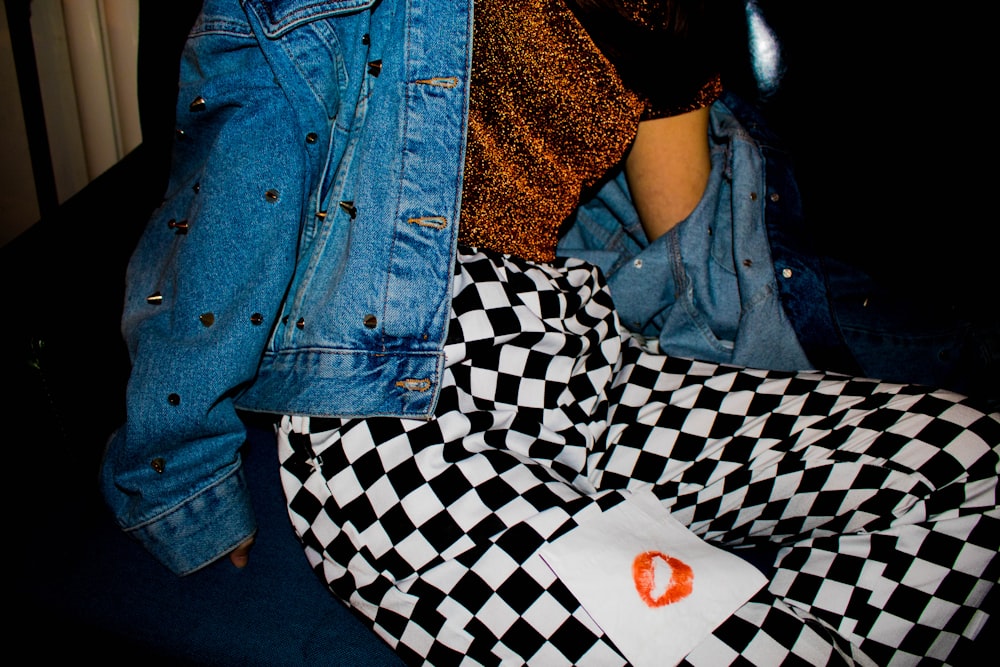 woman wearing black and white bottoms and blue denim jacket sitting on black surface