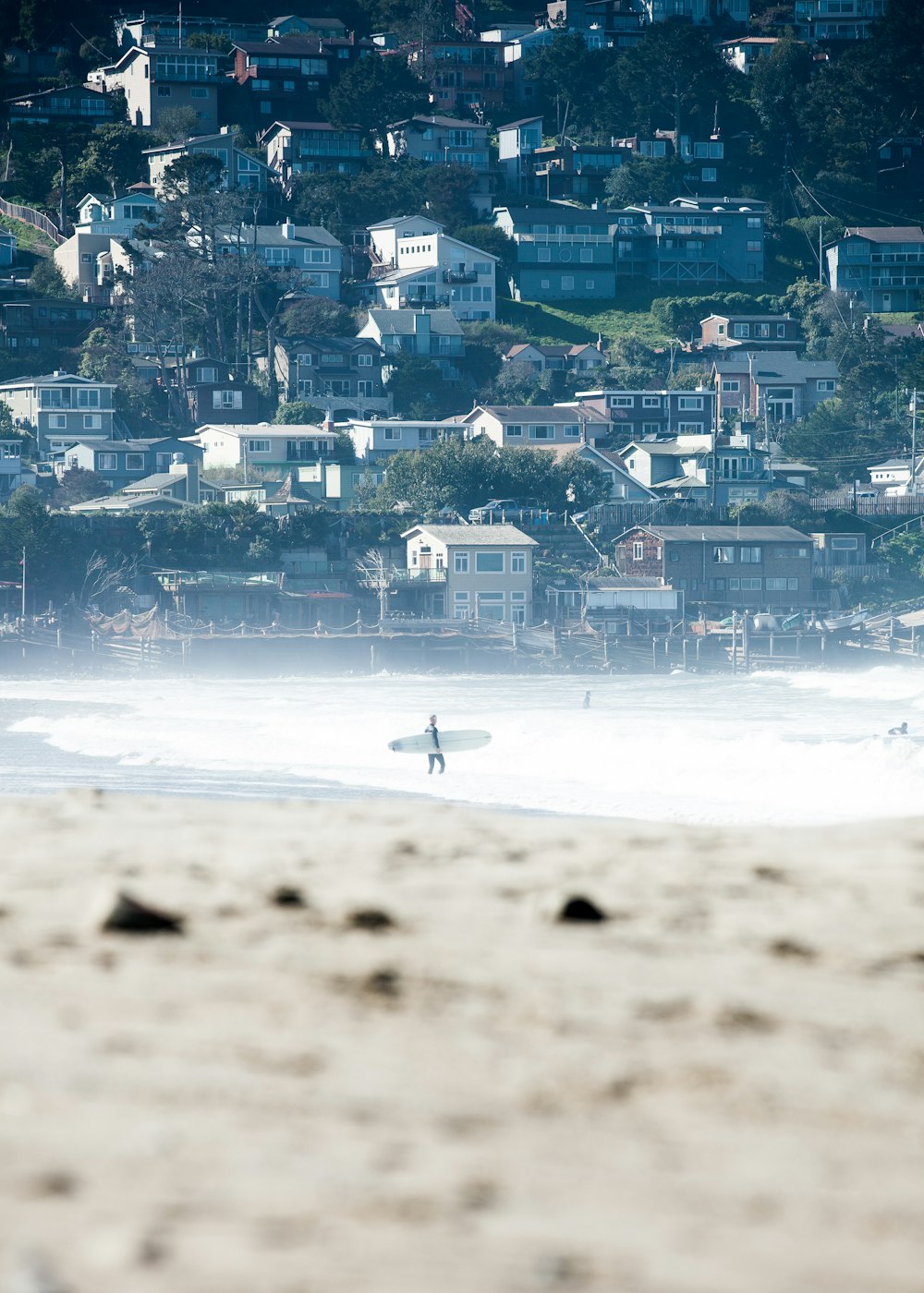 Persona che trasporta una tavola da surf bianca che cammina sulla battigia