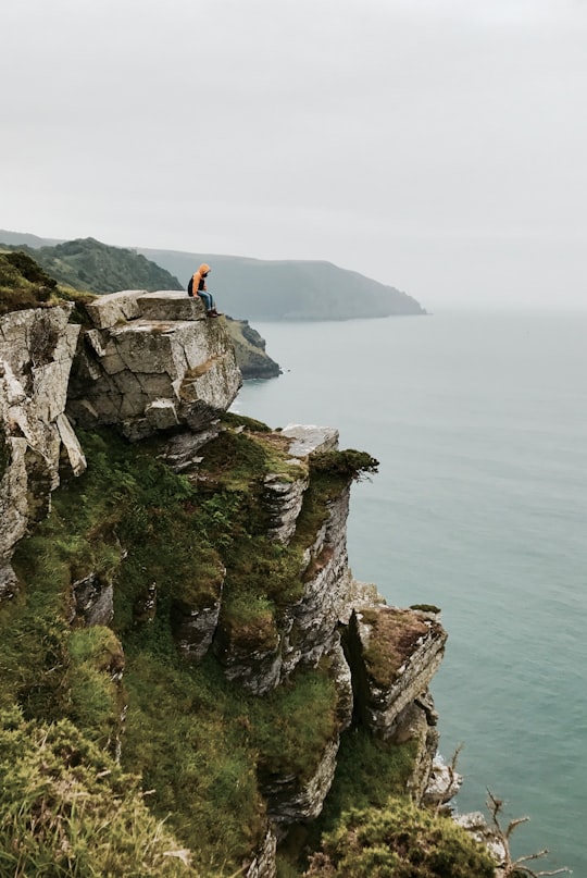 person sitting on cliffside during daytime in Valley of Rocks United Kingdom