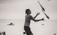 grayscale photo of man juggling on shore