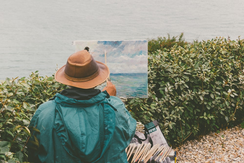 man painting body of water in front of bushes