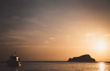 Sunset view over the ocean with silhouettes of the boat and island, glowing in warm tropical hues.