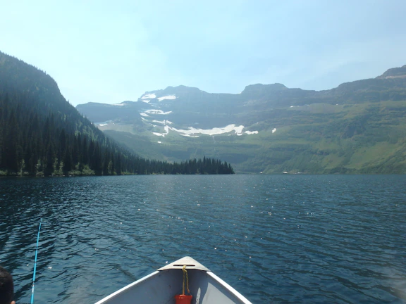 Angler casting a line into a serene mountain lake surrounded by lush greenery.