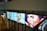 A series of three digital panels featuring artwork resembling portraits displayed along a wall in an interior setting. The portraits vary in artistic style, transitioning from pixel art to post-impressionism, each depicting a face with different expressions. Below the panels, glass doors and emergency exit signs are visible. A group of people appears in the background on the left side.