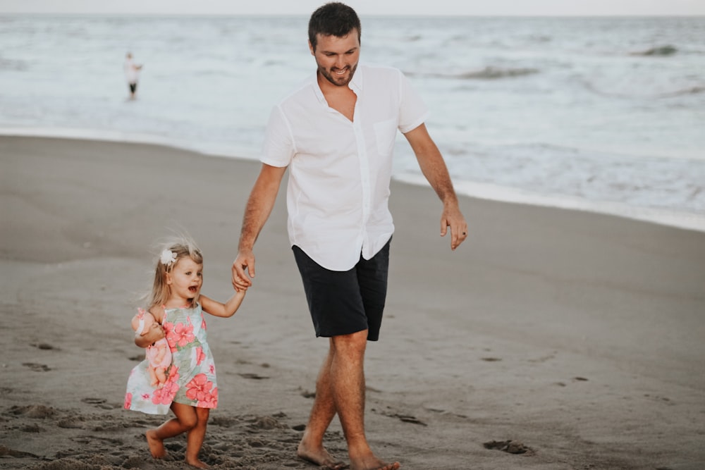 man holding her daughter while walking at the coastline