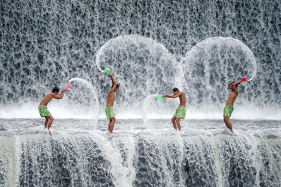 four men throwing dipper of water on waterfalls during daytime