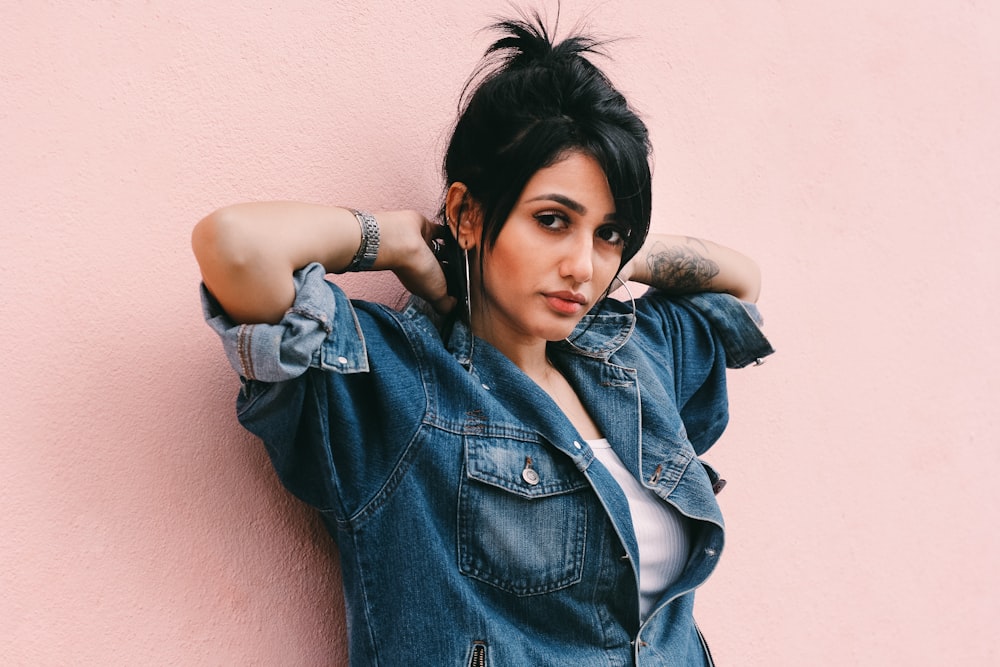 Woman wearing a denim wall leaning against a millennial pink wall