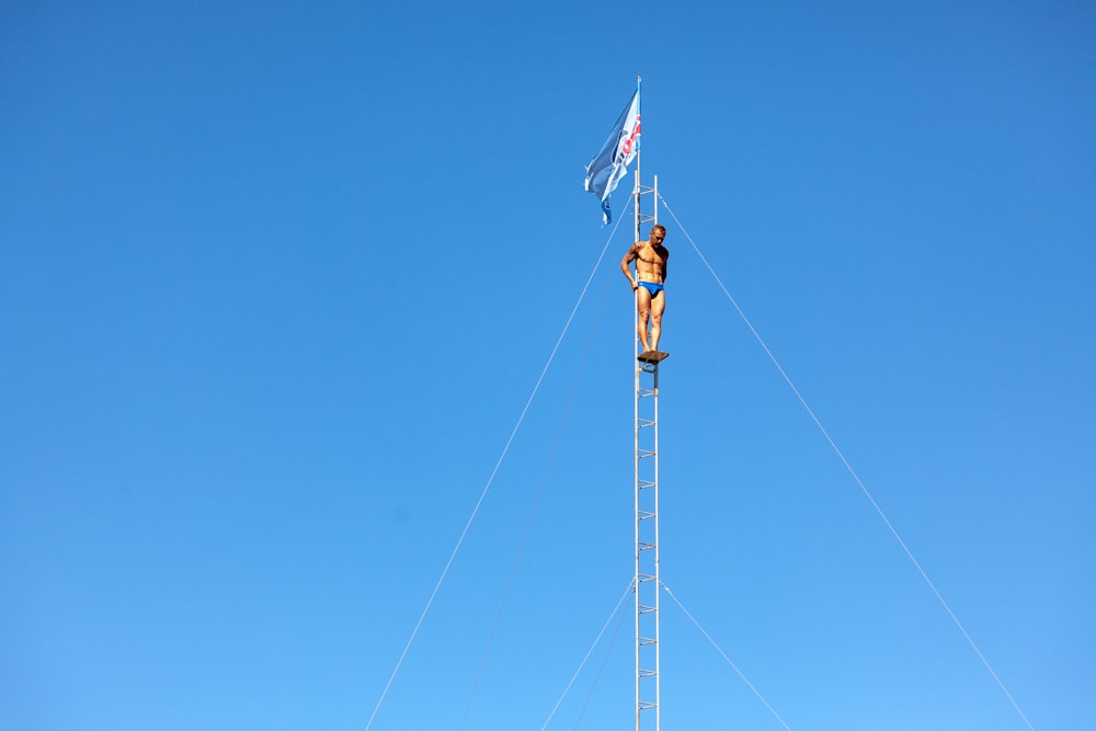 um homem em cima de um poste de metal ao lado de uma bandeira