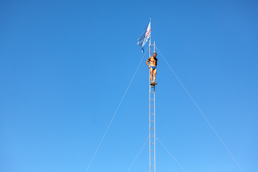 Un homme debout au sommet d’un poteau métallique à côté d’un drapeau