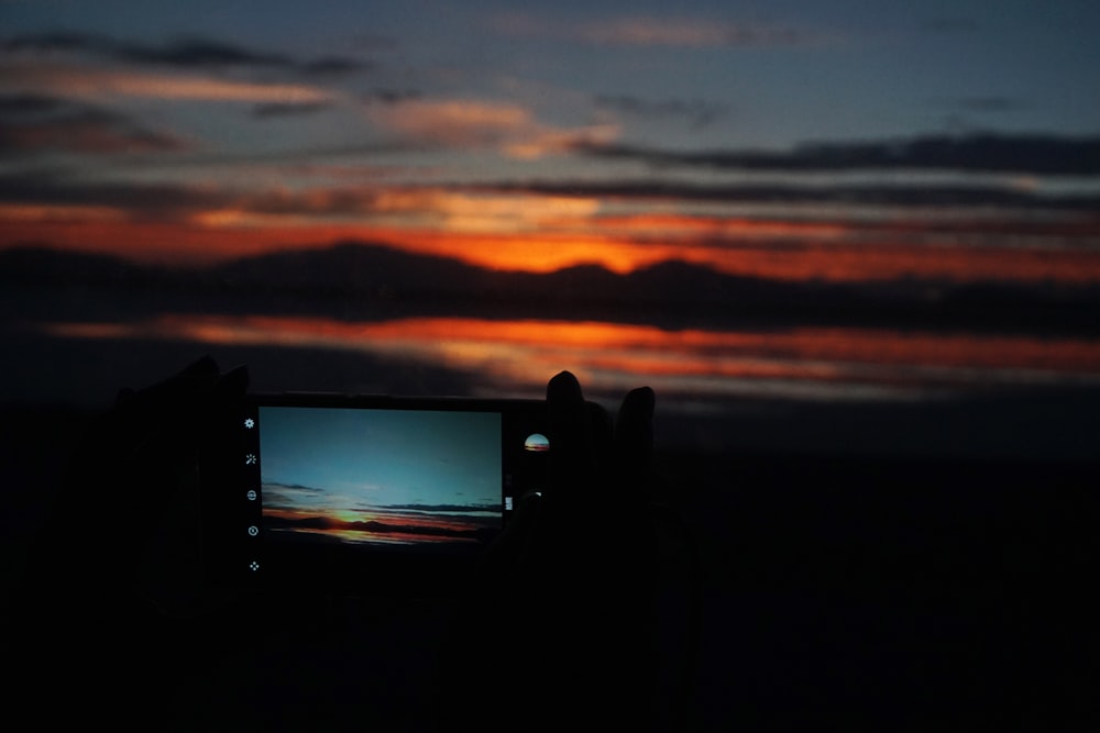 Fotografía de silueta de persona que captura la puesta de sol con teléfono inteligente