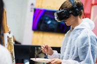 An artist interacting with a virtual reality headset surrounded by digital sculptures.