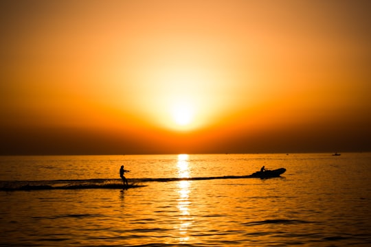 silhouette photo of man riding a motorboat with man surfboarding behind during golden hour in Lim Croatia