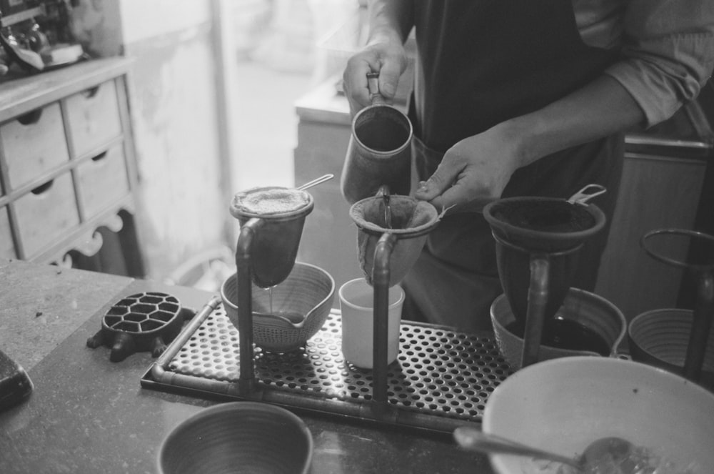 grayscale photo of person pouring water on strainer