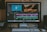 A computer monitor displays video editing software with multiple tracks of video and audio clips in a timeline. An image of aquatic life and another of a turtle are shown on the upper part of the screen. The workspace includes a keyboard, mouse, and external hard drive situated on the desk.