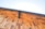 A close-up view of a wooden roof under a clear blue sky. The wooden planks are arranged in a layered pattern creating a warm, rustic aesthetic. The deep angle emphasizes the geometric structure, while a metal gutter runs along the edge.