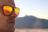 Close-up of a person wearing black Wild sunglasses against a sunlit mountain backdrop.