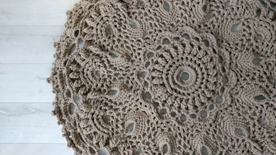Close-up of a delicate handmade crochet shawl in soft pastel colors draped over a rustic wooden chair.