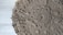 An intricately crocheted round doily with a detailed floral pattern, displayed on a light wooden floor. The texture of the yarn is coarse, giving it an artisanal look.