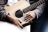Close-up of hands strumming an acoustic guitar during a vibrant band rehearsal.