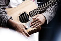 Close-up of hands playing an acoustic guitar with sheet music nearby.