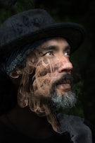 A person with a contemplative expression is looking upward, wearing a dark hat and a patterned bandana. A thick, swirling smoke effect overlays the image, adding a mysterious and surreal quality.